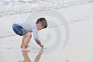 Happy asian little boy playing sand on tropical beach with happy smiling face on sunny day