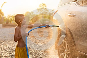 Happy asian little boy playing water from hose and spray to washing the car at outdoor in morning time