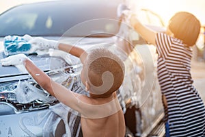 Happy asian little boy playing white soap and using blue sponge to washing the car at outdoor in sunset time