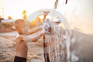 Happy asian little boy playing white soap and using blue sponge to washing the car at outdoor in sunset time