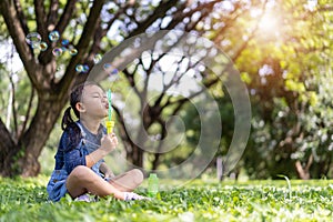 Asian little child girl blowing soap bubbles outside in green park