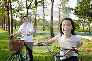 Happy asian little girl child with bicycle in outdoor park,smiling daughter with mother on a bike ride together,family activities