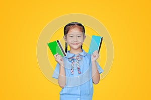 Happy Asian little girl in school uniform holding account book isolated on yellow background. Schoolgirl with bank passbook. Money