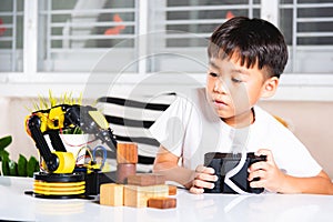Happy Asian little kid boy using remote control playing robotic machine arm for
