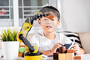 Happy Asian little kid boy using remote control playing robotic machine arm for pick up wood block