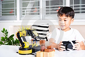 Happy Asian little kid boy using remote control playing robotic machine arm for pick up wood block