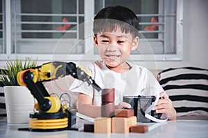 Happy Asian little kid boy using remote control playing robotic machine arm for pick up wood block