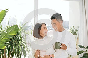 Happy Asian Lover kissing and hugging which holding a cup of water in living roo
