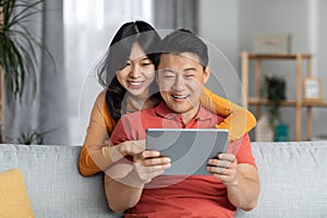 Happy asian lovers spending time together at home, using tablet