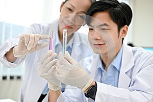 Happy Asian male scientist and senior female supervisor looking at the test tubes together