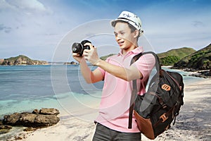 happy asian man backpacker taking photo with digital camera at the beach. travelling concept