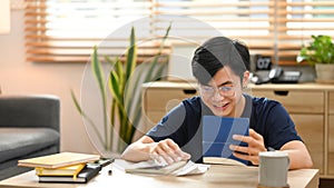 Happy asian man calculating money bank loan and managing expenses finances in living room. Household finance concept