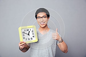 Happy asian man holding big clock and showing thumb up