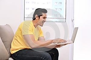 Happy asian man with laptop sitting on the couch