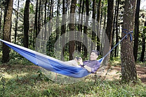 Happy asian man with smartphone lying in hammock