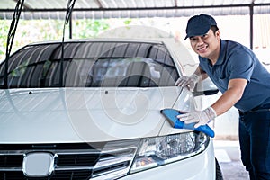 Happy asian man in uniform holds the microfiber in hand and polishes the car, Car wash service concept