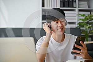 A happy Asian man wearing headphones, choosing music playlists on his phone