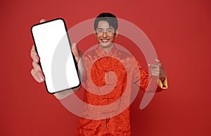 Happy Asian man wearing traditional dress showing mobile phone blank screen isolated on red background