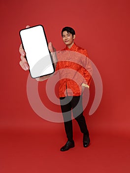 Happy Asian man wearing traditional dress showing mobile phone blank screen isolated on red background