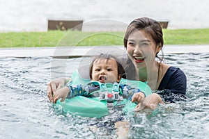 Happy Asian mom and baby playing in swimming pool using swim ring for leaning to swim relax in holiday. Vacation of family mother