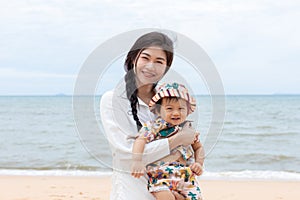 Happy Asian mom and baby smile looking at camera with beautiful sea. Vacation of family mother and baby spending time together