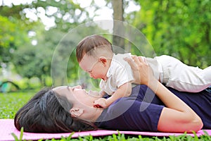 Happy Asian mom embrace her son lying in the green garden. Funny mother and infant baby boy playing in summer park