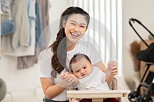 Happy asian mom playing and spending time with her newborn baby and looking at camera together at home.Adorable baby boy smile