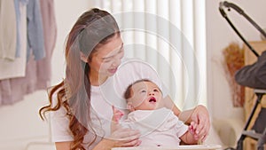 Happy asian mom playing and spending time with her newborn baby and looking at camera together at home.Adorable baby boy smile