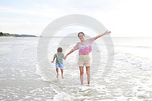 Happy Asian mom and son at tropical sand beach with waving hands. Happy family mother and little boy having fun in summer holiday