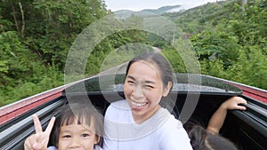 Happy asian mother and children standing up and waving through car sunroof.