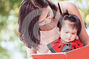 Happy asian mother and cute little baby girl reading a book