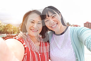 Happy asian mother and daughter taking selfie photo for postin on social network - Family people having fun with technology trends