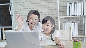 Happy Asian mother and little daughter to participate e-learning online education class with laptop computer and raising hands tog