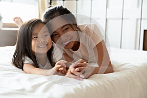 Happy Asian mother lying in bed together with small daughter