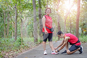 Happy asian mother and son tying shoe laces in the park