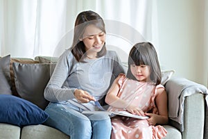 Happy asian mother teaching her cute kid daughter to studying at home