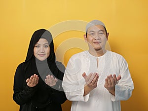 Happy Asian muslim couple making pray to God, dua or do`a gesture, hands raised up, Islamic culture