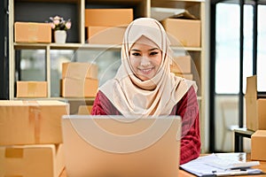 A happy Asian Muslim female online seller replying customers questions on the shopping website