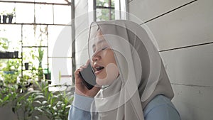 Happy Asian muslim woman talking on phone outside of her home, smiling happy cheerful
