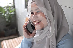 Happy Asian muslim woman talking on phone outside of her home, smiling happy cheerful