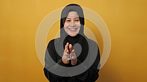 Happy Asian muslim woman wearing hijab, happy proud clapping gesture, half body portrait on yellow