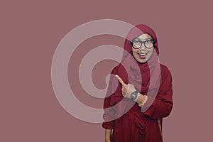 happy Asian muslim woman wearing red hijab and pointing at copy space