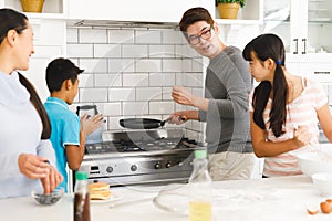 Happy asian parents with son and daughter preparing breakfast in kitchen and talking