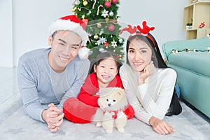 Parents and their little daughter lying on ther floor with a little dog at living room,decorated by christmas tree photo