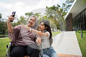 Happy Asian patients in a wheelchair use smartphones to take pictures with careful caregivers or nurse Concept of happy retirement