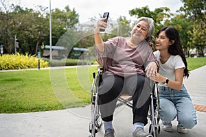 Happy Asian patients in a wheelchair use smartphones to take pictures with careful caregivers or nurse Concept of happy retirement