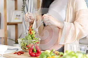 Happy asian pregnant woman cooking salad at home, doing fresh green salad, eating many different vegetables during pregnancy,