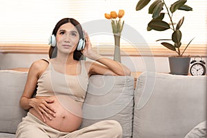 Happy Asian pregnant woman sitting on the bed listen to music in headphones