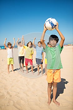 Happy Asian preteen boy posing with ball at beach