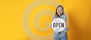 Happy asian pretty woman in casual clothing smiling and hold open sign board with copy space area for text on yellow background, s